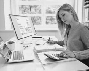 Une comptable qui travaille sur la digitalisation de ses factures. Elle regarde en direction de son bureau et est en train de taper à la calculatrice.
