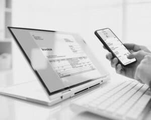 Une photographie représentant la facture électronique. À gauche un ordinateur où est affichée une facture électronique et à droite une main tenant un téléphone
