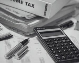 Une image en noir et blanc comprenant une calculatrice, un livre sur la fiscalité, un stylo ainsi que divers documents.